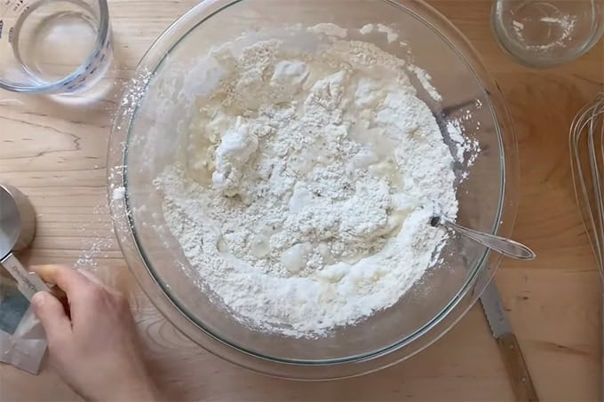 Water added to a bowl of flour, salt, baking powder, and butter.
