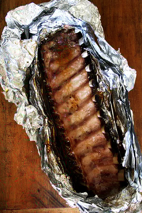Full rack of oven-cooked baby back ribs in foil on wooden surface