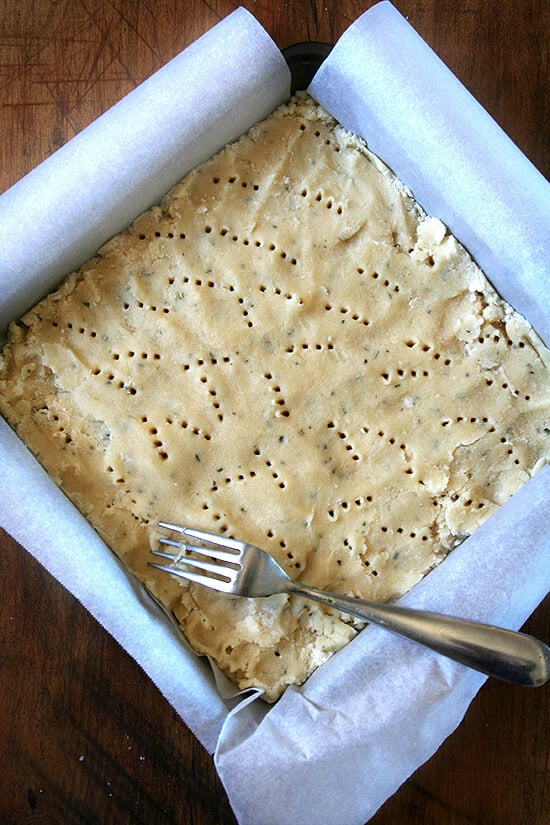 shortbread ready for the oven A square baking dish filled with rosemary shortbread dough, pricked with a fork.