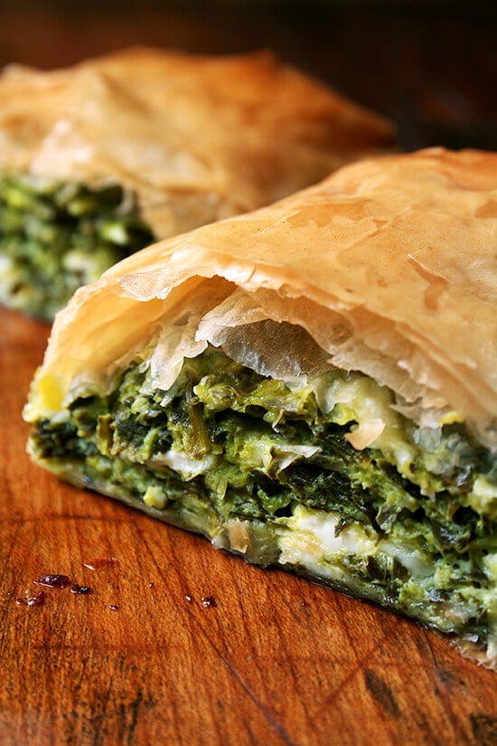 When baked in strudel form, spanakopita assumes an almost breakfast croissant-like character, a perfect bundle of flaky pastry, egg, cheese, and greens. Yum. // alexandracooks.com A halved spanakopita strudel on a board.