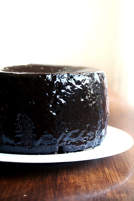This cake is everything a chocolate cake should be: fudgy, moist, intensely chocolaty. When assembled into layers with chocolate ganache slathered in between, it becomes the perfect birthday finale for any chocolate lover. As a half recipe topped with black velvet icing, it can be an elegant dessert, a perfect treat to whip up if you find yourself hurricane housebound (with any luck with your power still on) or to snack on with your morning coffee! // alexandracooks.com Double Chocolate Cake with Black Velvet Icing on a plate, ready to be sliced.