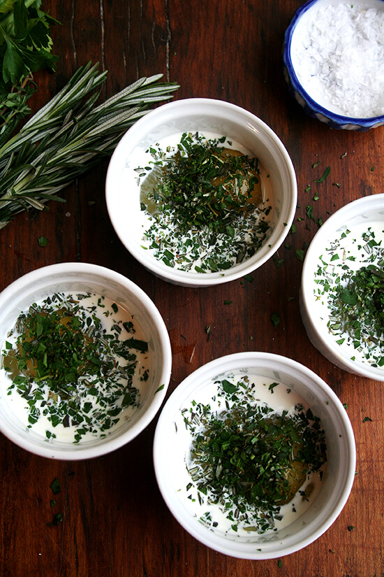 4 ramekins, each holding an egg, cream, and herbs.