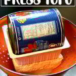 A homemade tofu press with a colander and a can of tomatoes.