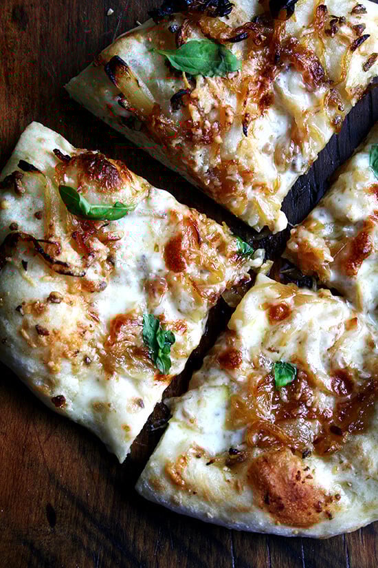 A just-baked caramelized onion and burrata pizza sprinkled with basil cut into wedges. 