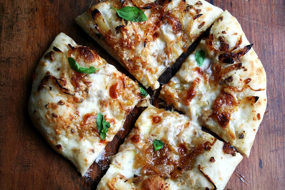 A just baked caramelized onion and burrata pizza sprinkled with basil, cut into wedges.