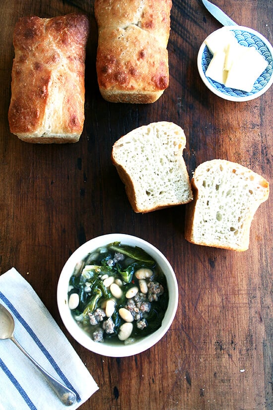 This bone-warming, white bean soup derives its flavor from the classic Italian combination of greens and beans as well as spicy Italian sausage. Nothing could be more comforting than a big bowl of this soup with a hunk of crusty bread. // alexandracooks.com A bowl of white bean, sausage, and escarole soup aside homemade peasant bread.