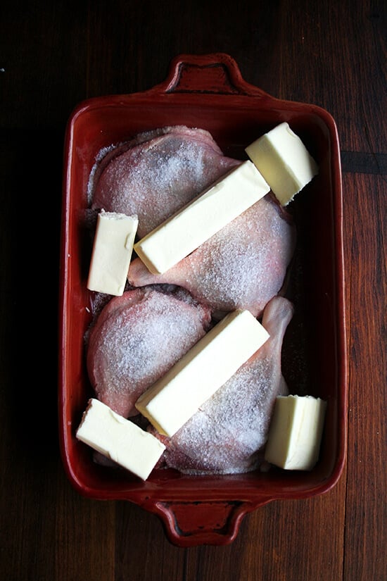 Four duck legs in a 9x13-inch red baking dish sprinkled with salt and covered with a pound of butter.