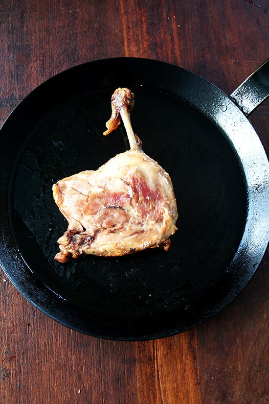 A duck leg confit in a cast iron skillet.