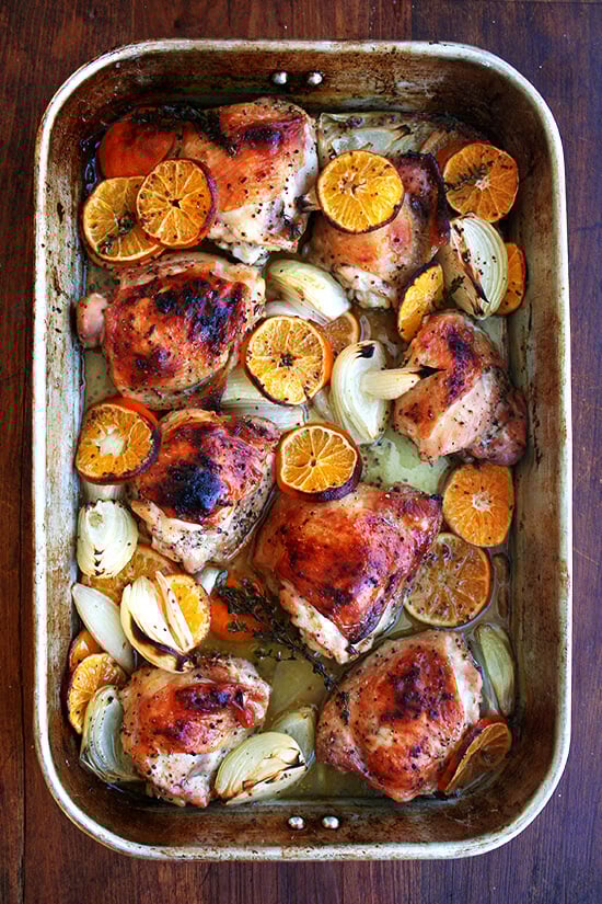 A roasting pan with roast chicken and clementines.