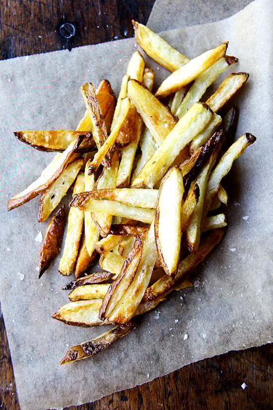 Every summer, when the potatoes start arriving in our CSA, I am blown away by their flavor, by how they need nothing more than olive oil and salt. This recipe for oven fries is especially good, especially crispy on the edges, especially creamy on the inside. // alexandracooks.com A pile of just-baked homemade French fries.