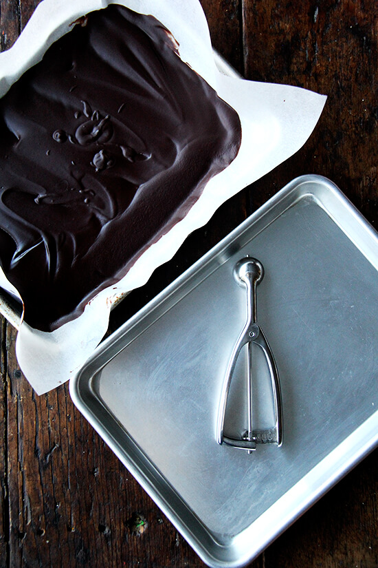 Truffle batter in parchment lined baking sheet aside empty baking sheet with a #100 scoop resting inside.