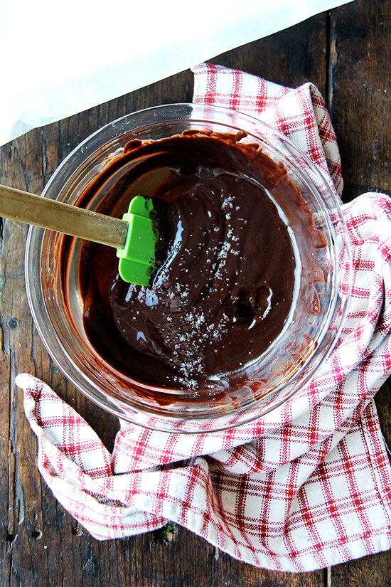 A bowl of melted chocolate, sprinkled with sea salt, with a spatula inside.