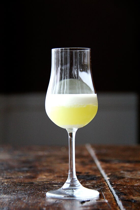 This recipe for limoncello is a two-phase process, but is very simple. It makes a great gift and thus far has been very well received. I like to drink it topped with heavy cream. Yum. // alexandracooks.com A glass filled with homemade limoncello topped with heavy cream.