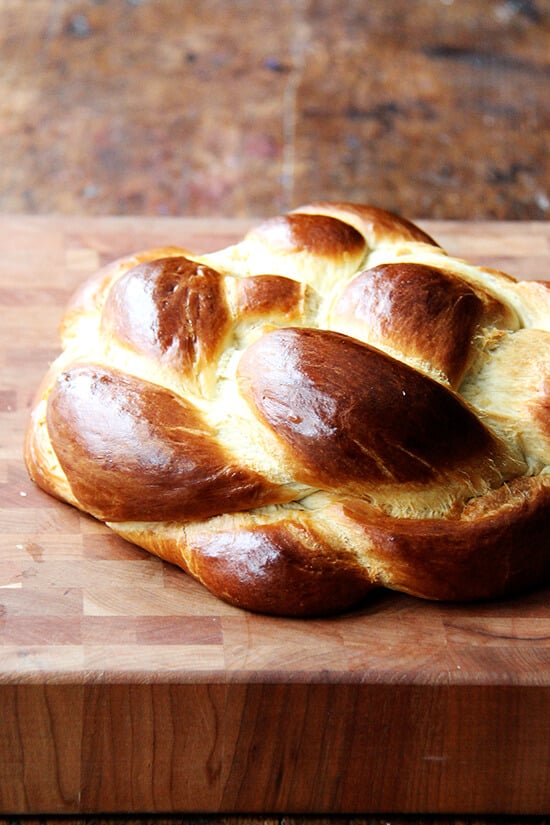 This simple challah rises beautifully and bakes into a perfectly golden, light and airy, tangle of braids. I like to make this often as a treat aside any soup and a treasure for weekend brunch.// alexandracooks.com A cutting board with a loaf of challah bread on top.