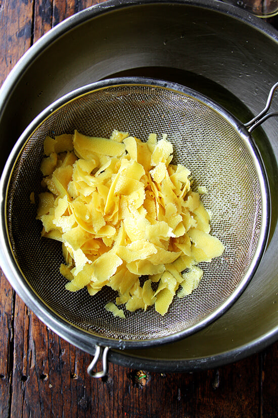 A strainer filled with petrified lemon zest over a bowl holding Everclear alcohol.