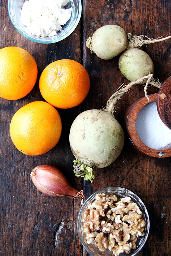 Watermelon radishes on a board with goat cheese, salt, walnuts, and shallots.