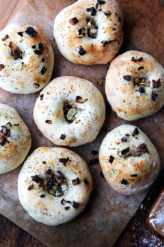 Every batch of bialys disappears quickly — the onion-poppy seed-breadcrumb filling/topping, whose flavor permeates the whole bialy, is irresistible. Later in the day we halve them and spread them with softened butter or cream cheese. For dinner we toast them under the broiler, one half covered with a slice of cheddar, and then, upon pulling them from the oven, we slide a fried egg onto the uncheesed half and hit it with a healthy squirt of Sriracha. // alexandracooks.com Just baked bialys on a board.