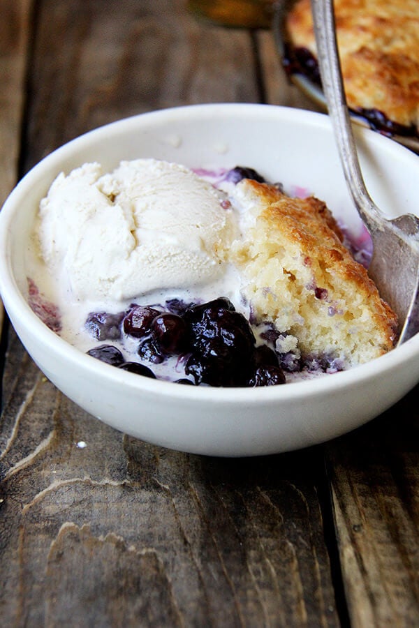 The idea behind this blueberry cobbler is that the blast of heat from the bubbling berries helps cook the underside of the biscuits, while the hotter temperature of the oven nicely browns the top. The result? An evenly cooked — not dry! — tender, golden biscuit. // alexandracooks.com A close-up shot of a bowl of blueberry cobbler with ice cream.