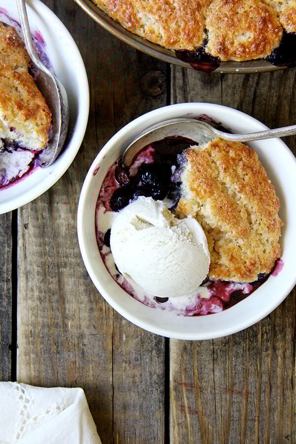 The idea behind this blueberry cobbler is that the blast of heat from the bubbling berries helps cook the underside of the biscuits, while the hotter temperature of the oven nicely browns the top. The result? An evenly cooked — not dry! — tender, golden biscuit. // alexandracooks.com A bowl of blueberry cobbler with ice cream.