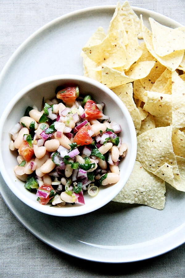 We've been eating this white bean and orange salsa, mixed with onions, lime, jalapeƱos, cilantro, and orange, with chips, but it would be nice tucked inside a taco or a burrito or aside spicy wings and nachos and anything else you might find yourself surrounded by on game day. // alexandracooks.com A bowl of white bean salsa aside chips.