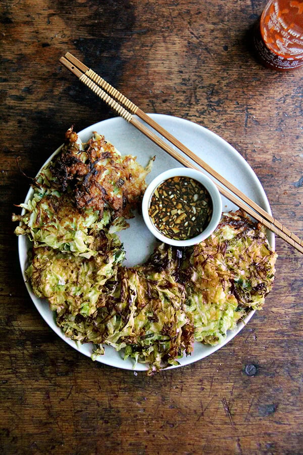 Okonomiyaki, Japanese cabbage pancakes, can be made in countless ways: okonomiyaki essentially means prepared as you like. This my favorite version I've made yet, but know that you can add to it as you like with shrimp or chicken, sesame seeds or bonito flakes, other vegetables, etc. I prefer a soy-based dipping sauce to the more traditional mayonnaise-based, and, like the corn fritters, find these as irresistible freshly fried as cold straight from the fridge. // alexandracooks.com A plate of okonomiyaki with soy dipping sauce.