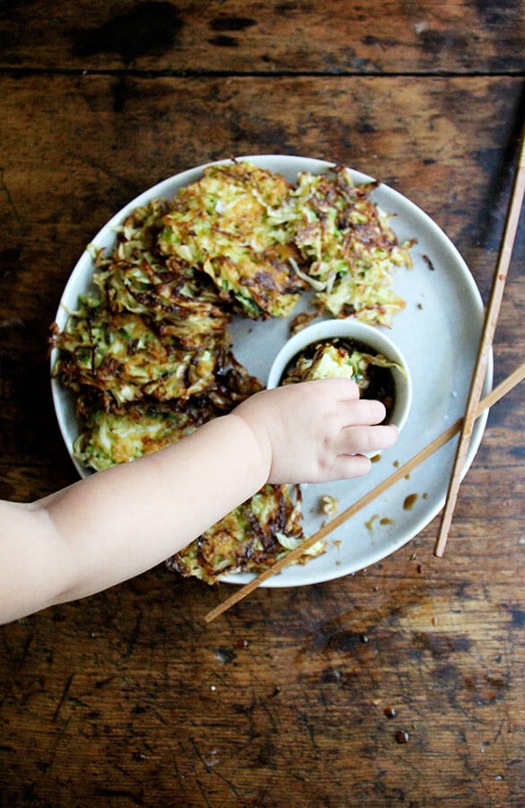 Overhead shot of child dipping a cabbage pancake into a soy dipping sauce.