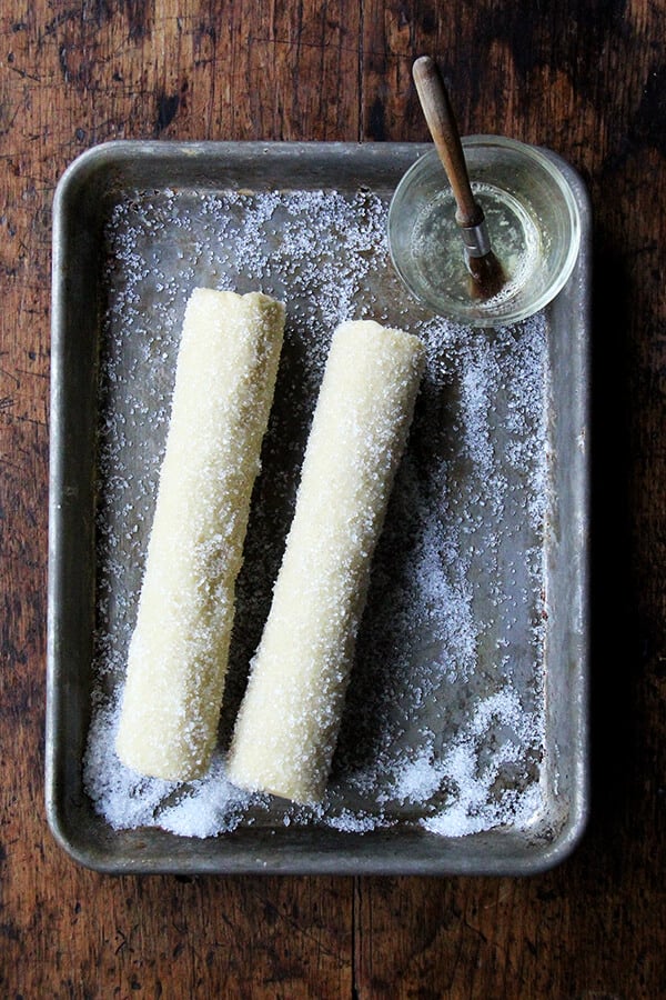 Two logs of sablé cookie dough on a small sheet pan rolled in decorative sparking sugar.