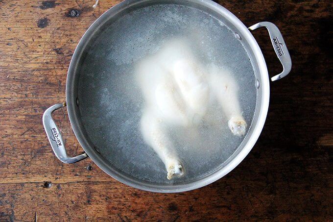 A chicken poaching in a large pot.