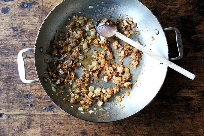 An overhead shot of a sauté pan with onions and spices (ras-el-hanout).