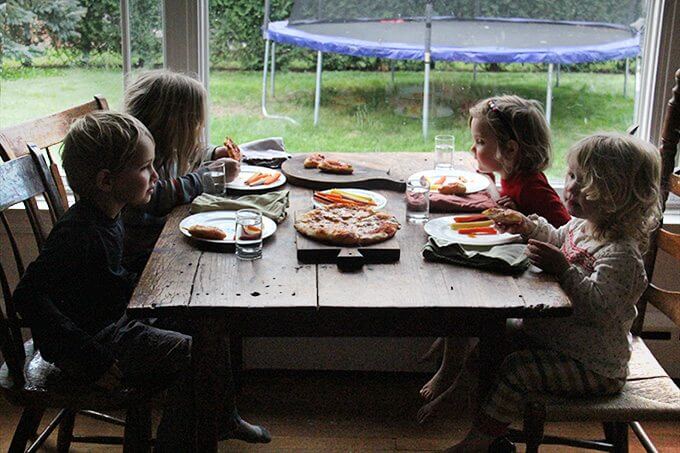 Sideview of 4 kids eating skillet pizza and carrots.
