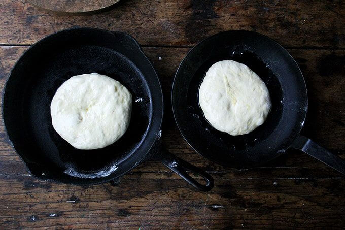 Two cast iron skillets holding pizza dough.