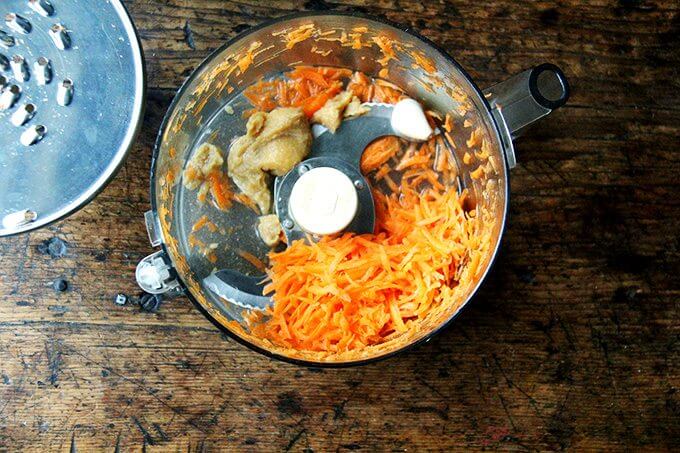 A food processor with shredded carrots, miso, and garlic.
