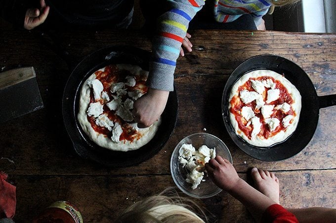 Three kids top two cast iron skillet pizzas.