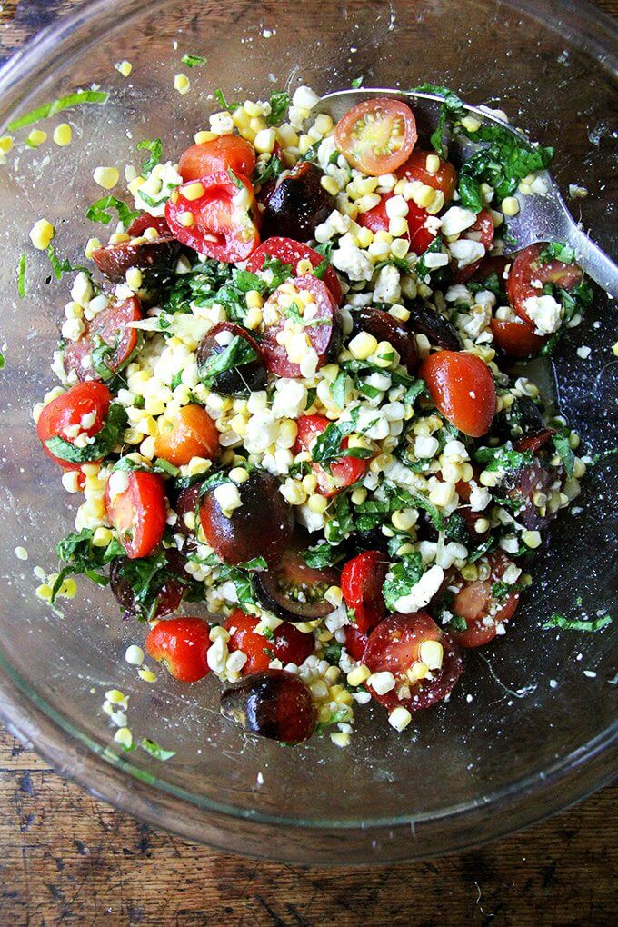 In this corn salad, raw corn doesn’t mind rubbing elbows with all of its seasonal pals. Here, it’s tomatoes and herbs, but the simple formula could be riffed on endlessly: diced bell peppers, cilantro, scallions, cubes of raw zucchini or roasted eggplant, diced mozzarella, Cheddar or Monterey Jack cheese would all work well here. // alexandracooks.com A bowl of raw corn salad with tomatoes and feta.