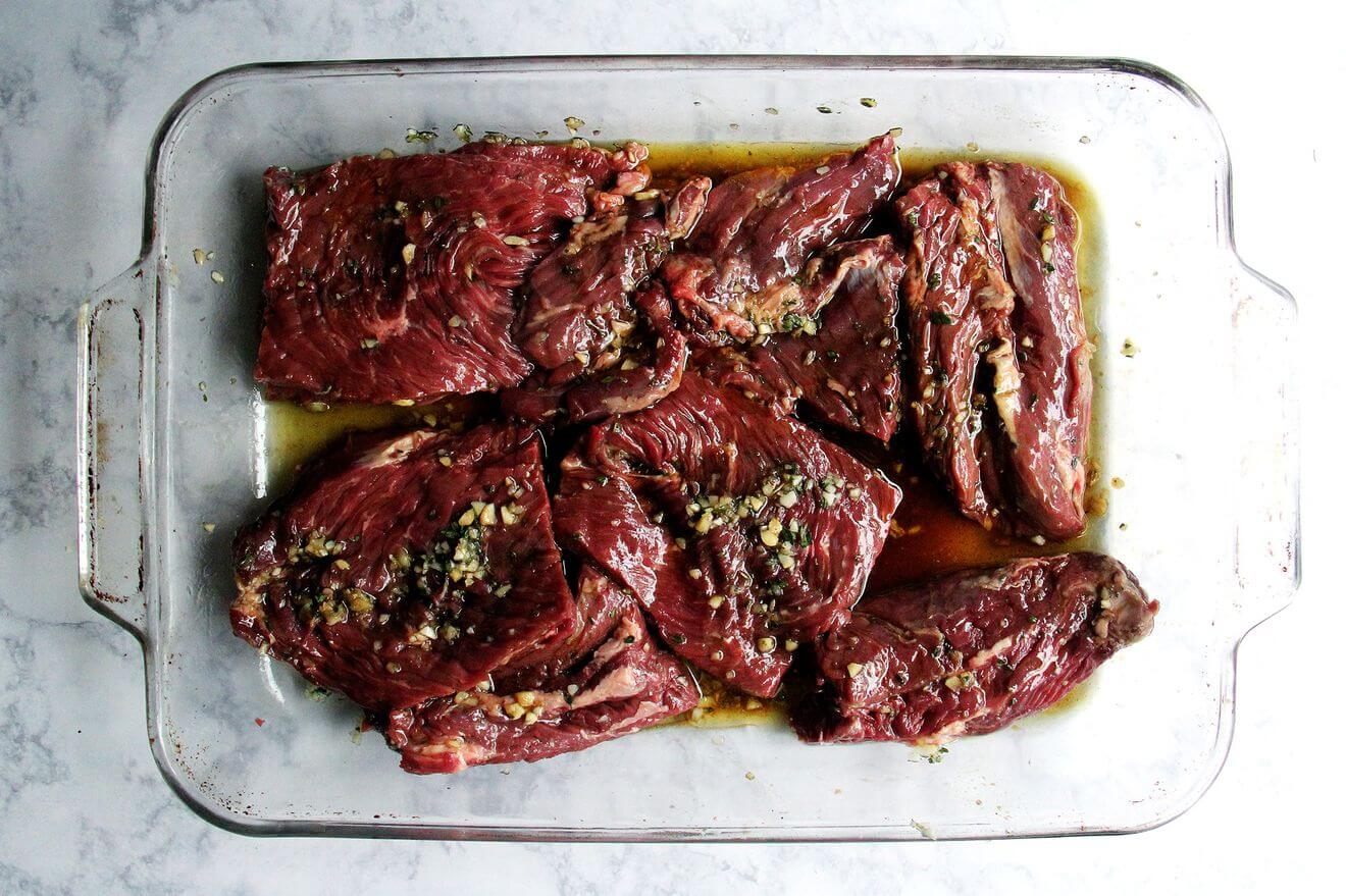 A 9x13-inch pan holding hanger steak marinating in garlic, worcestershire, thyme, and olive oil.