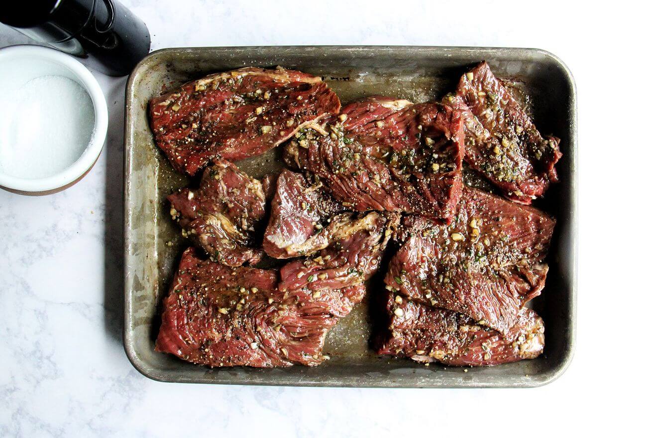 A sheet pan holding marinating hanger steaks, salt, and pepper.