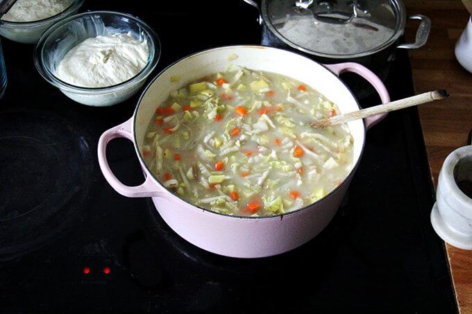 An overhead shot of a stovetop holding a large pot of cabbage soup and two bowls of rising bread dough.