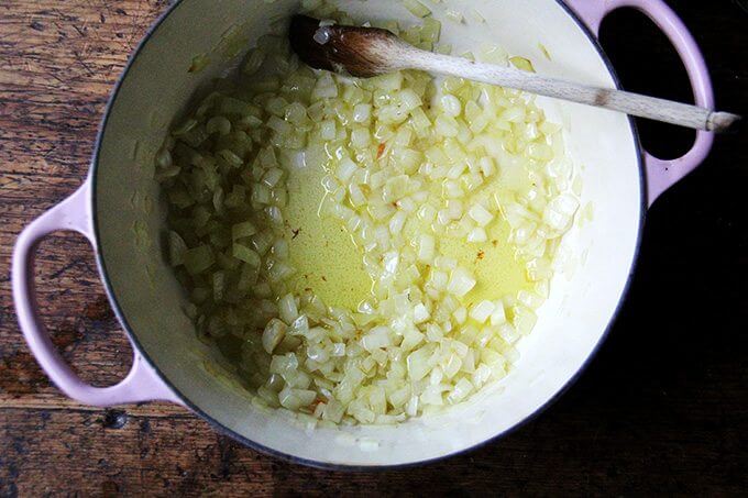 An overhead shot of a large pot holding olive oil and onions being sautéed.