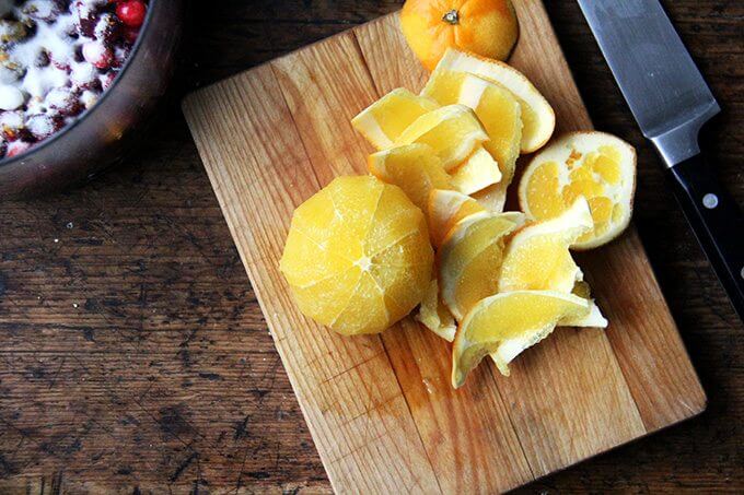 A cutting board with a peeled orange on top aside a knife.