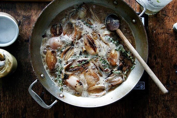 Shallots in a skillet with white wine and thyme.