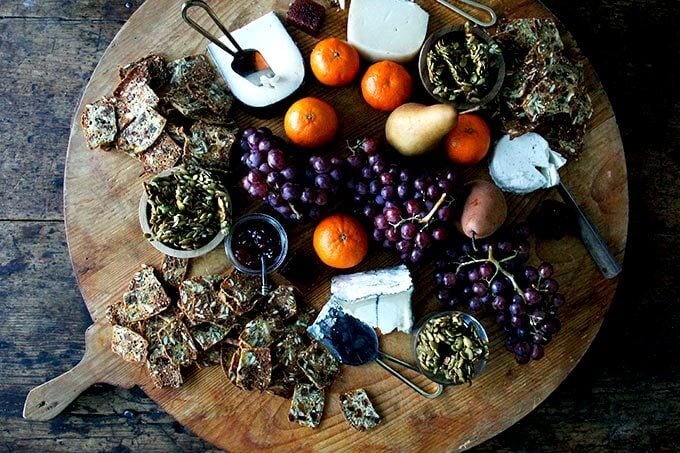 A cheese board loaded with homemade three-seed crackers, grapes, oranges, pears, and candied pepitas.