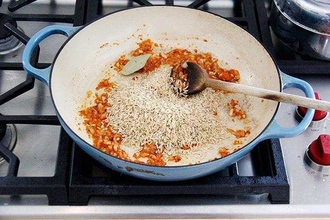 A skillet with uncooked rice, harissa, onion, and garlic.