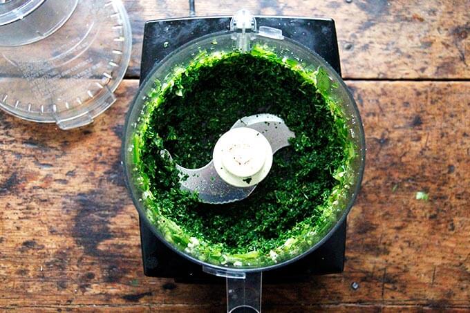 A food processor filled with puréed herbs, garlic, and chilies.