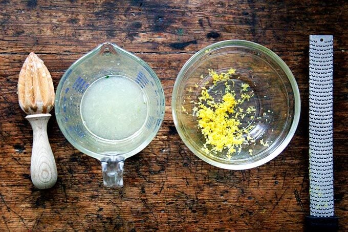 A liquid measure filled with lemon juice aside a bowl filled with zest.