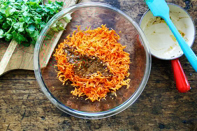 A large bowl filled with grated carrots and warm harissa dressing.