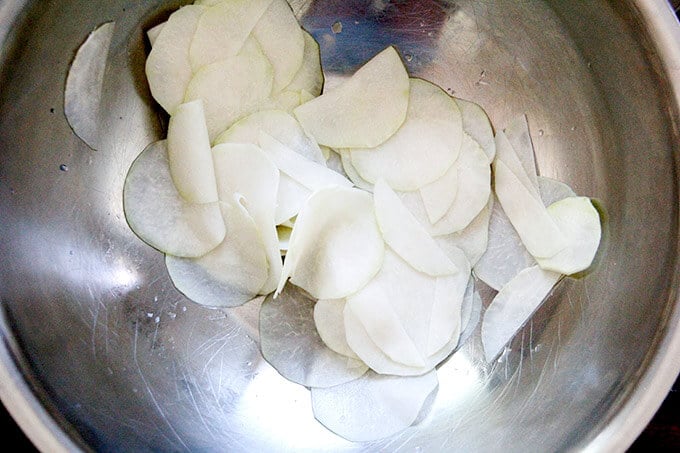 Kohlrabi, thinly shaved, in a bowl with salt.