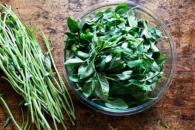 A bowl of basil leaves aside stems on a table.