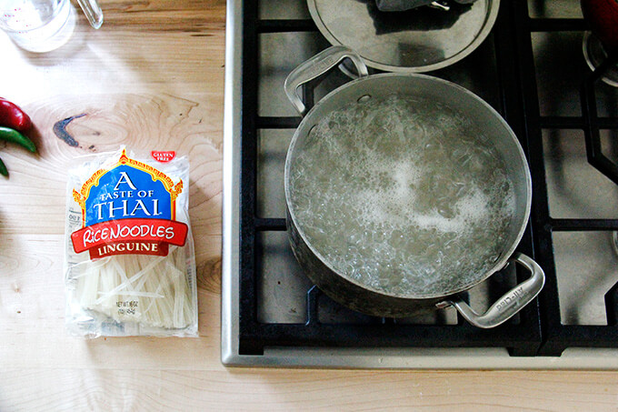 A stovetop with a pot of boiling water aside a package of rice noodles.