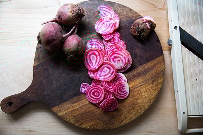 A board with sliced, raw, Chioggia beets, aka candy stripe beets aside a mandoline.
