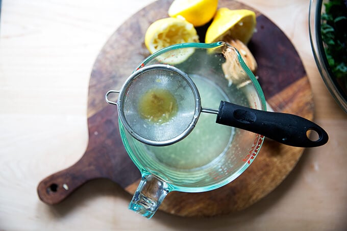 A small stainer set over a liquid measure with juiced lemons on the side.